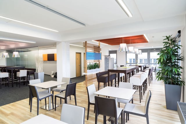 Betriebsrestaurant mit weißen Tischen, dunklen und hellen Stühlen und einer Palme