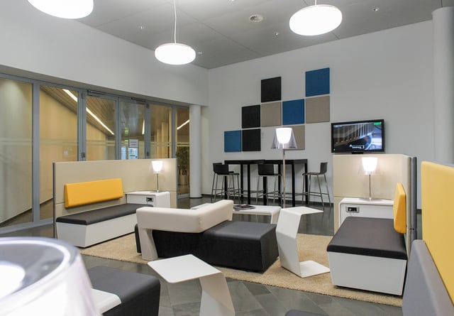 Lounge mit Sitzbänken, Stehtisch mit Barhockern und einer Wand mit blauen und grauen Akustikpaneelen