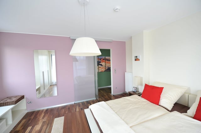 Schlafzimmer mit Doppelbett, roten Kissen und rosa Wand mit Spiegel