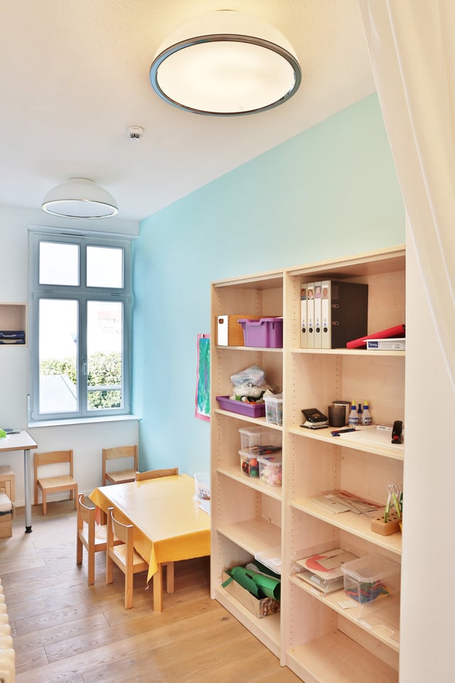 Raum mit hellblauer Wand, Holzregal und Kindertisch mit Stühlen
