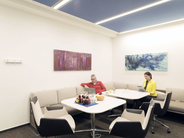 Besprechungsecke mit Eckbank und Tischen, ein Mann und eine Frau arbeiten an Laptops
