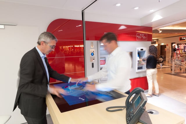 Zwei Männer an einem Tisch mit Touchscreen, im Hintergrund Automaten