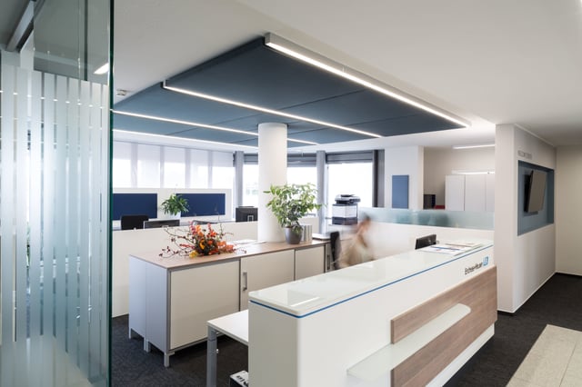 Blick über eine Empfangstheke mit Blumenstrauß auf die Arbeitsplätze dahinter