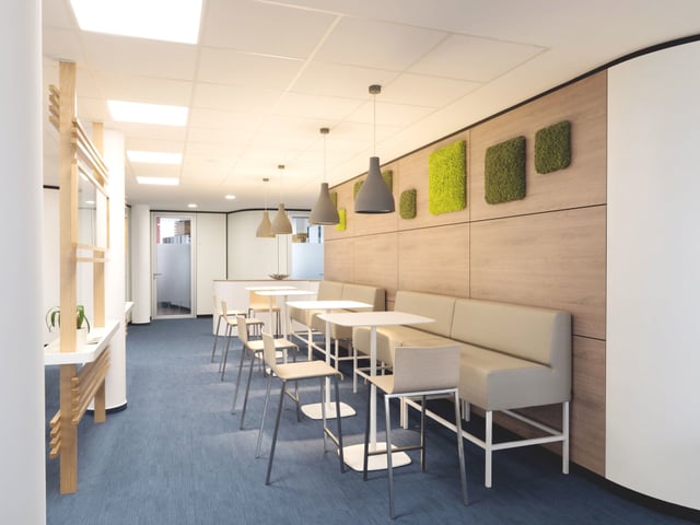 Langer Raum mit Sitzbank an einer Holzwand mit Moosbildern, Stehtischen und Pendelleuchten