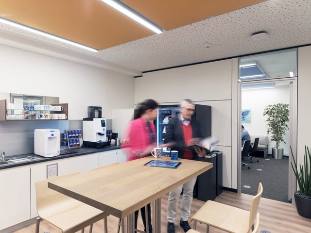 Teeküche mit Stehtisch aus Holz, zwei Personen am Getränkeautomaten