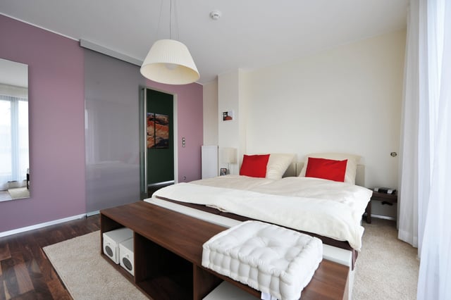 Schlafzimmer mit Doppelbett, roten Kissen und Holzbank am Bettende
