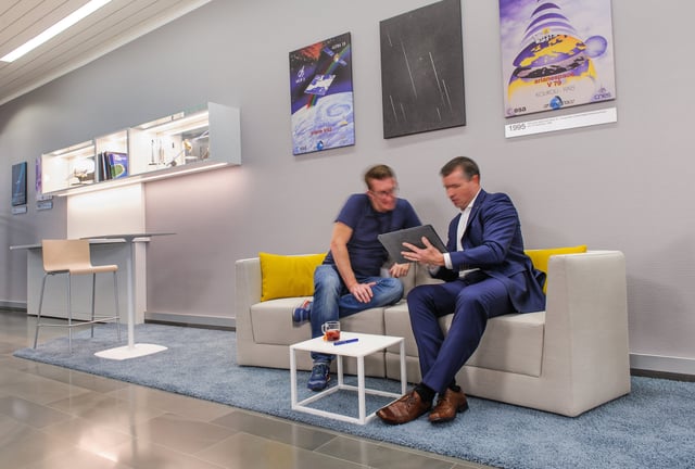 Zwei Männer auf einem hellen Sofa mit gelben Kissen schauen auf ein Tablet