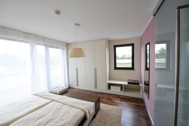 Schlafzimmer mit Doppelbett, Einbauschrank und bodentiefen Fenstern mit Vorhängen